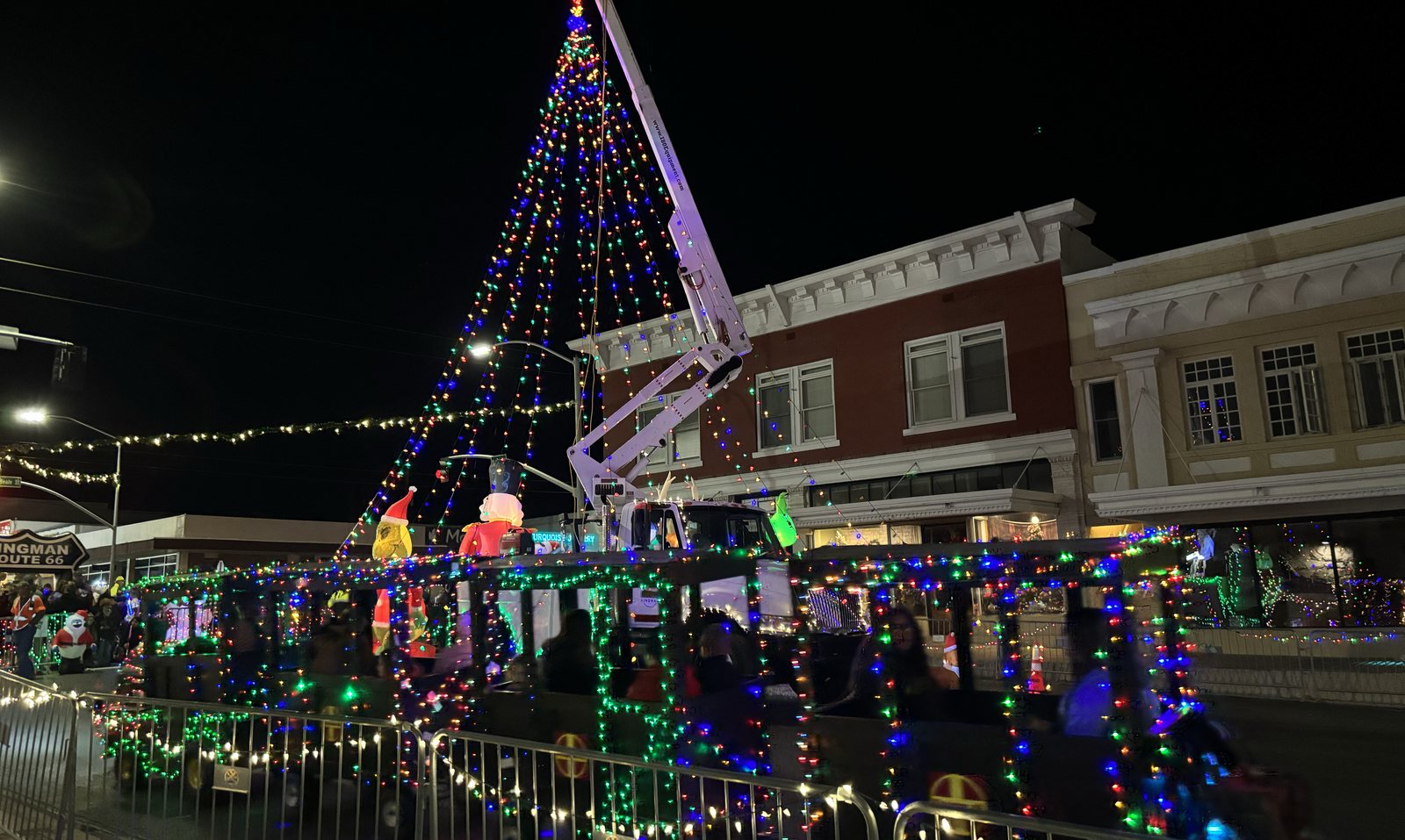 A lit Christmas tree raised over Beale Street with downtown storefronts behind it