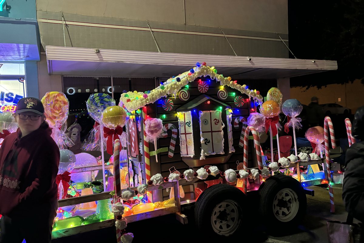 A parade float built as a candy shop, covered in lights and oversized lollipops